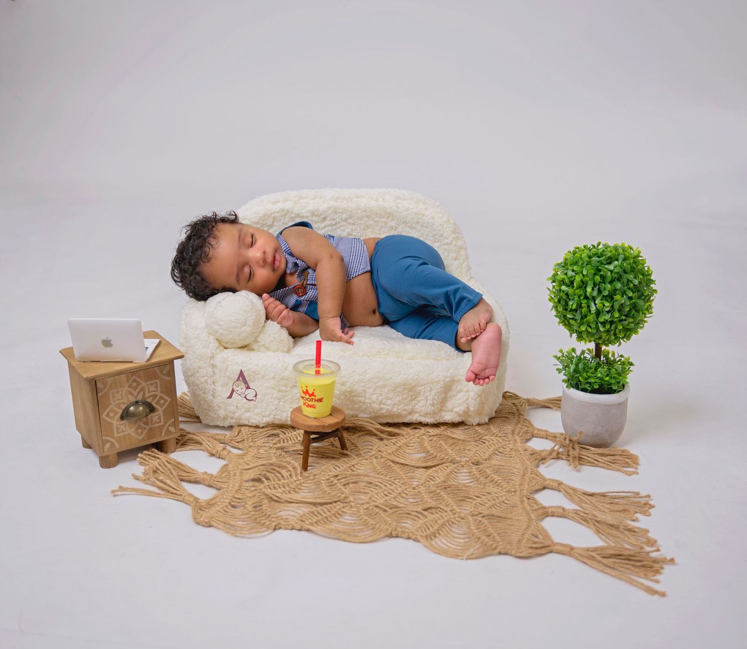 Baby sleeping on cream cushions with decorative props and green plants.