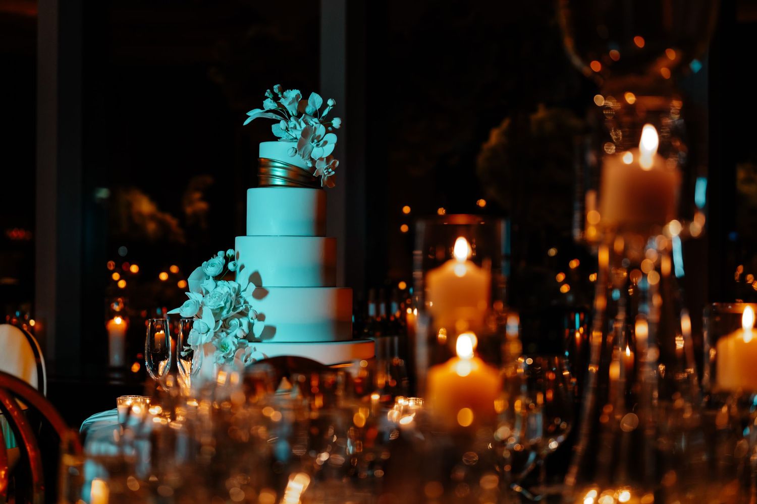 Romantic reception setup with turquoise wedding cake and glowing candlelight.