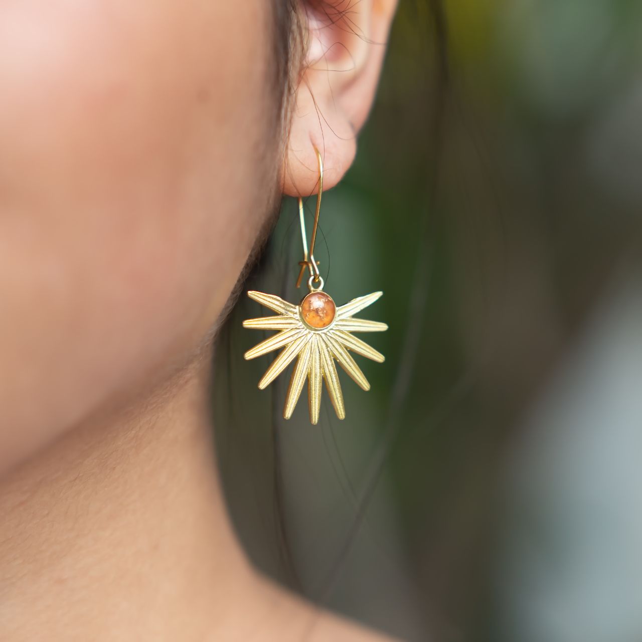 sun-shaped fine jewelry earring in a blurred background