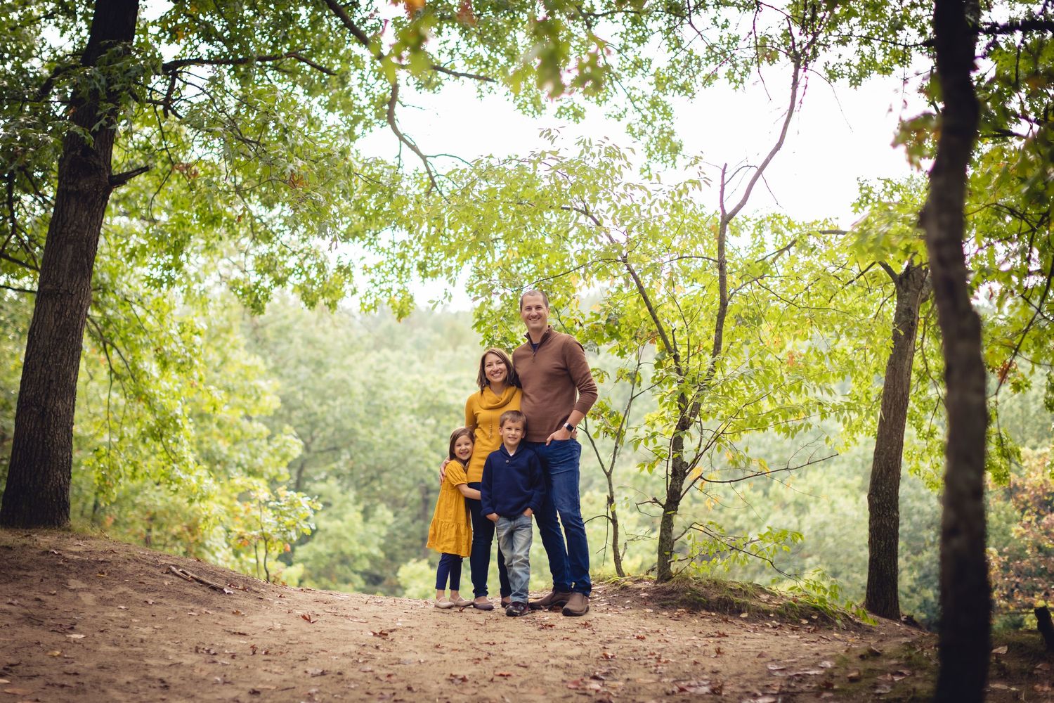 Family wearing coordinating outfits embraces while standing on autumn forest trail.