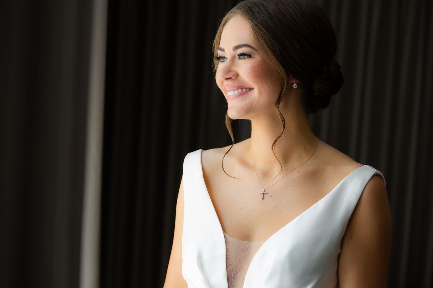 Bridal portrait with classic white dress against dark background with window lighting.