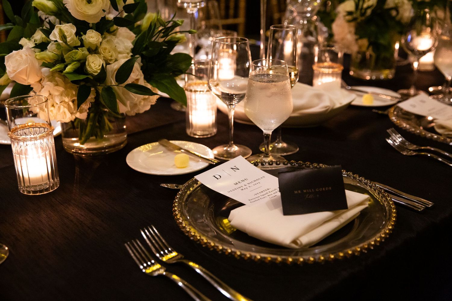 Fine dining place settings with gold-rimmed chargers and glowing candle centerpieces.
