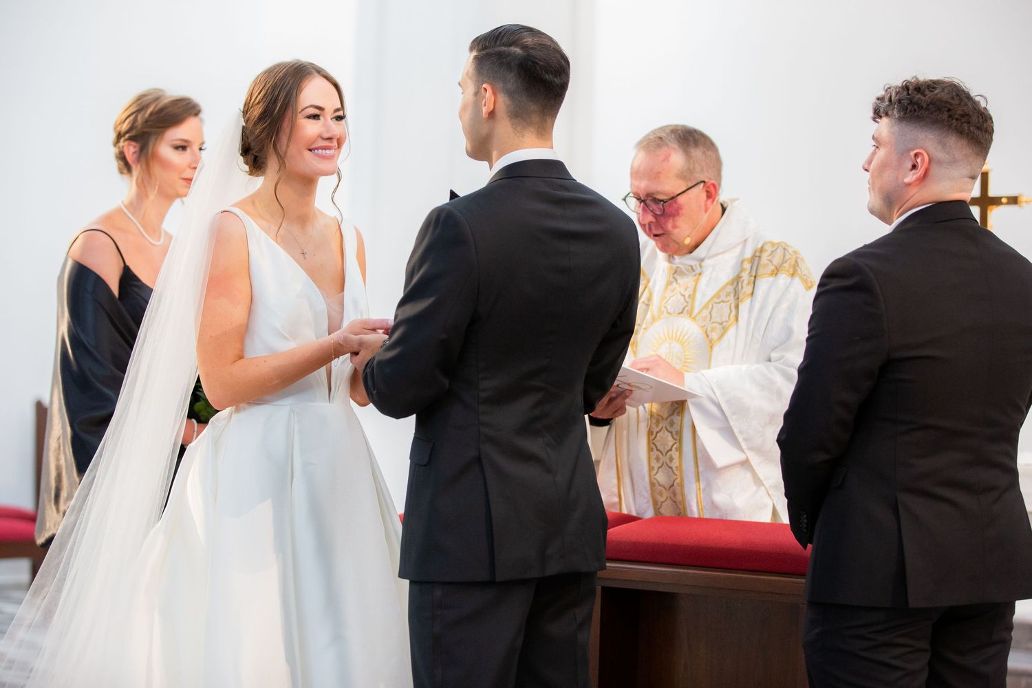 Wedding ceremony proceedings at church altar with geometric wall pattern in background.
