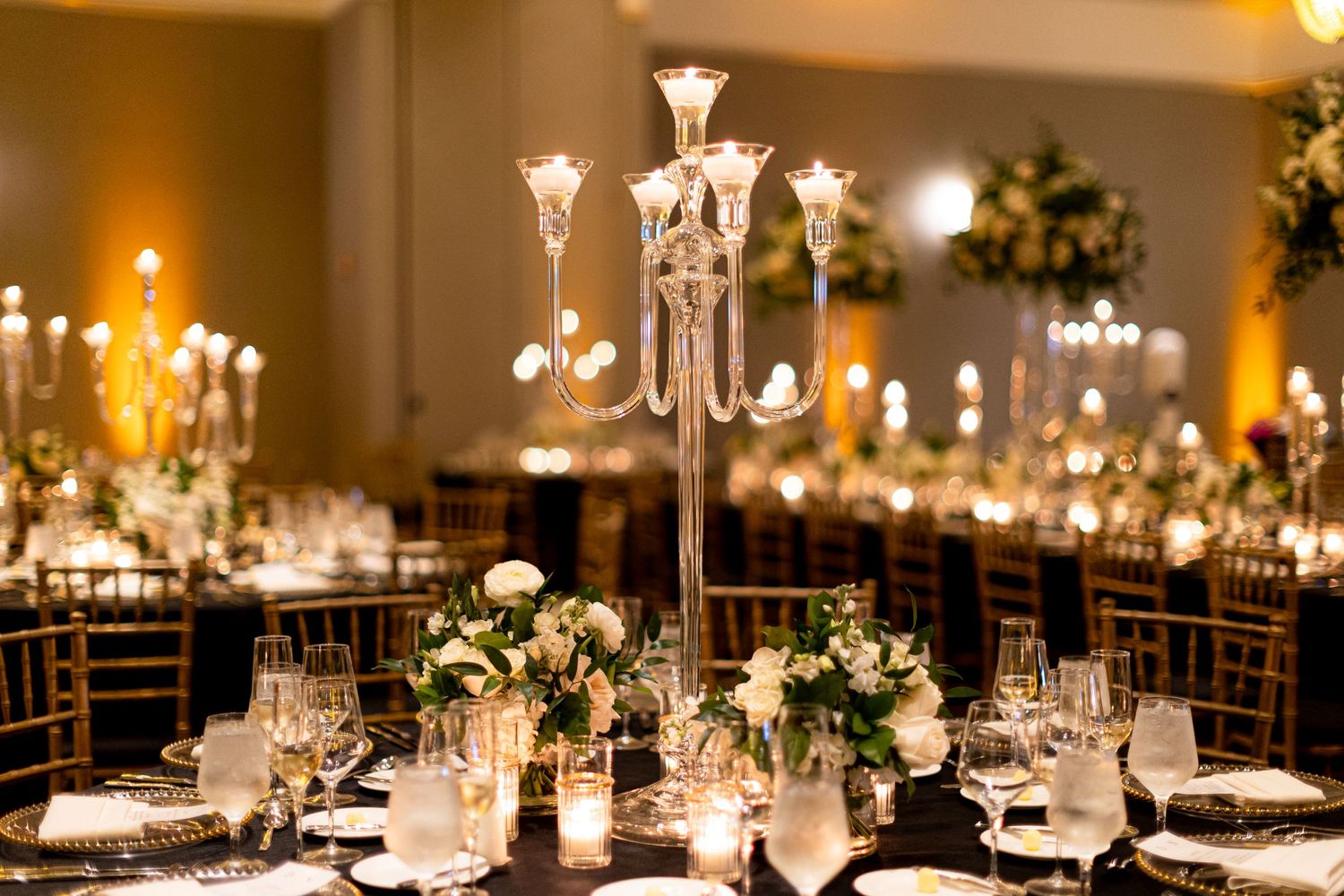 Luxurious wedding reception tables set with crystal chandeliers and warm ambient lighting.