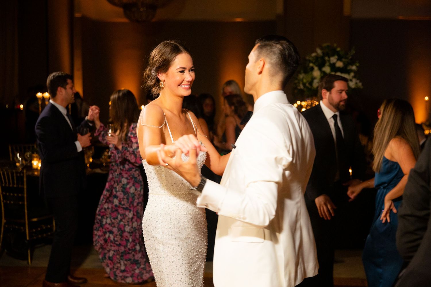 Wedding guests dancing and celebrating on a dimly lit dance floor.