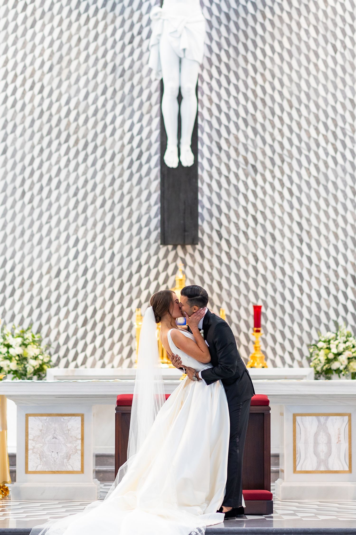 A couple shares an intimate moment during their wedding beneath a modern church crucifix.