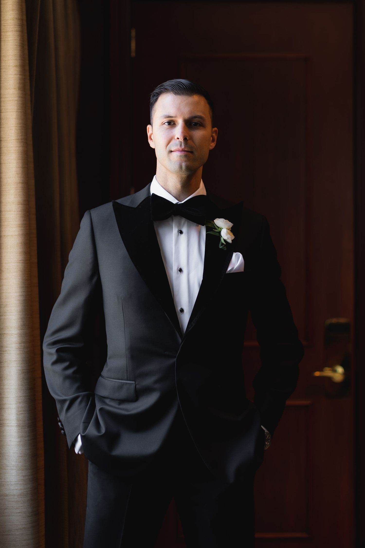Men in classic black tuxedos and bow ties stand in an elegant venue.