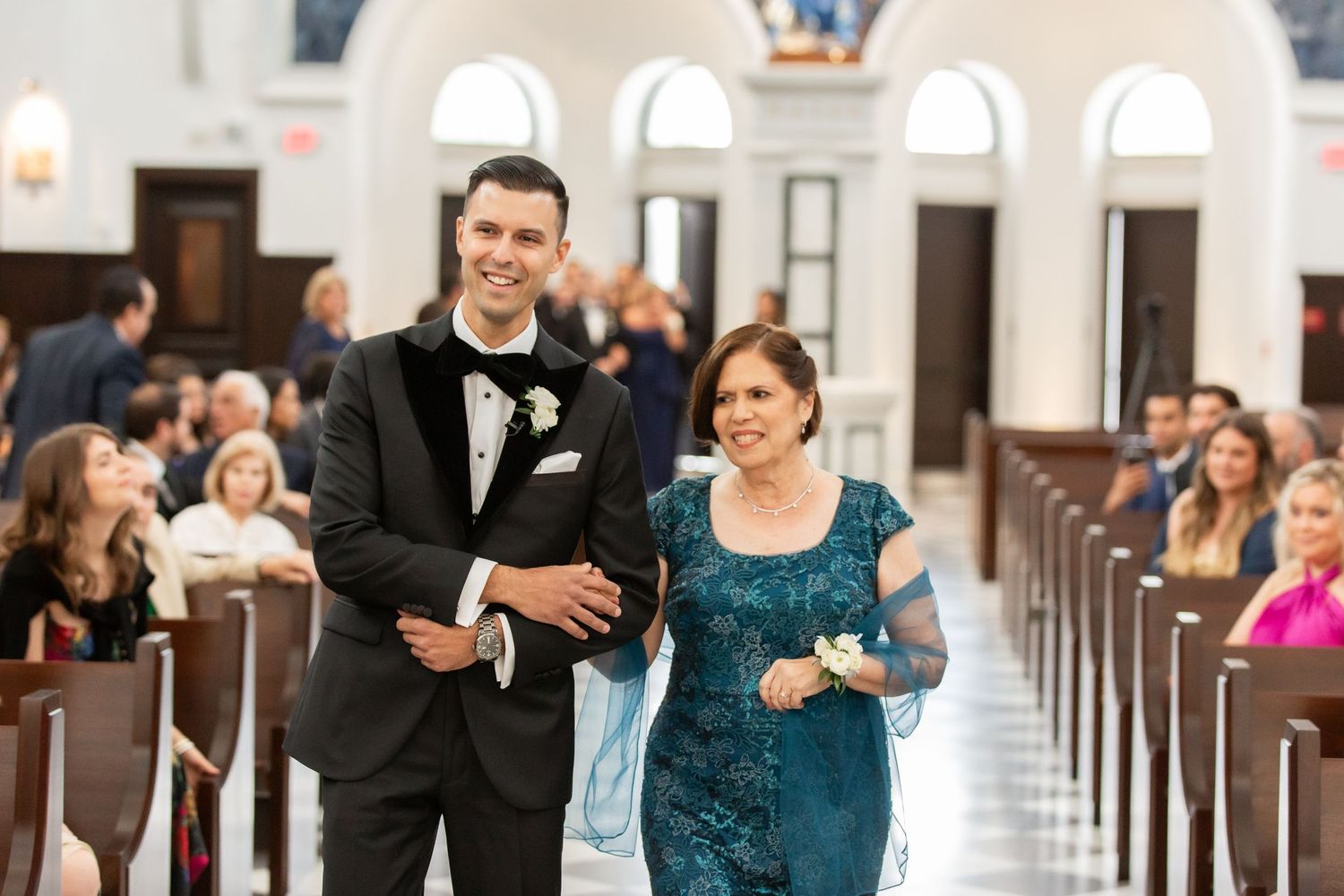Wedding party members in formalwear walking down a church aisle with black and white checkered floors.