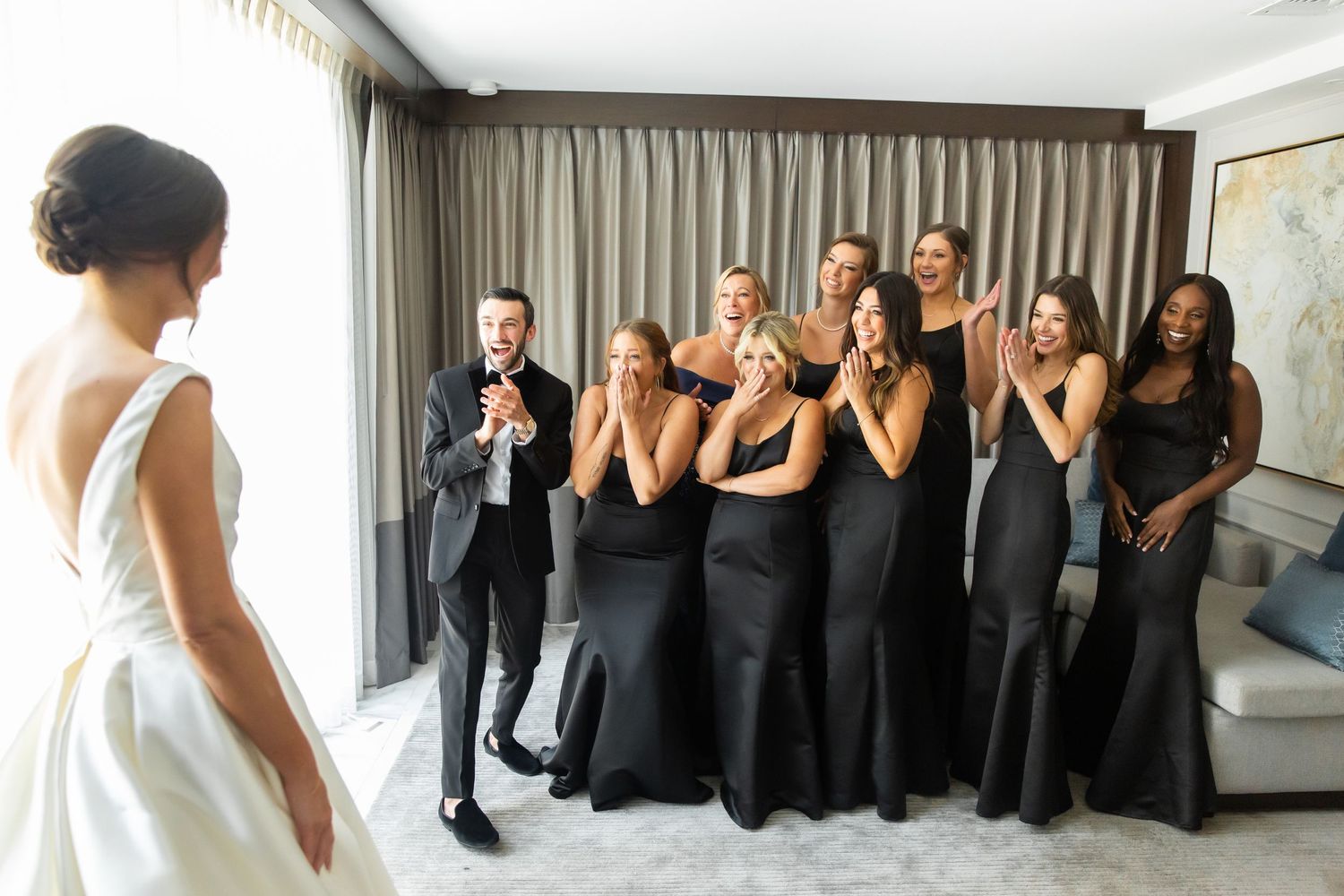 Wedding party members in black and white attire pose emotionally together in a room.