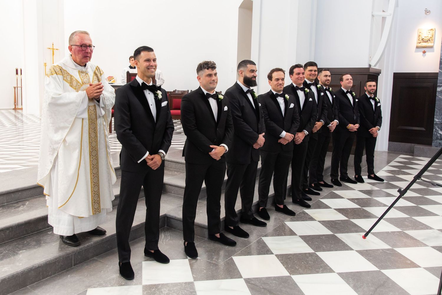 Groomsmen lined up in black tuxedos during formal wedding ceremony in church.