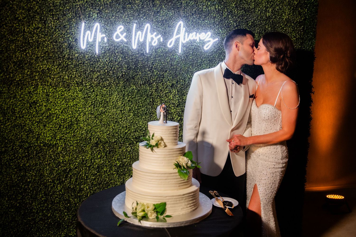Romantic moment between newlyweds next to their wedding cake with neon signage.