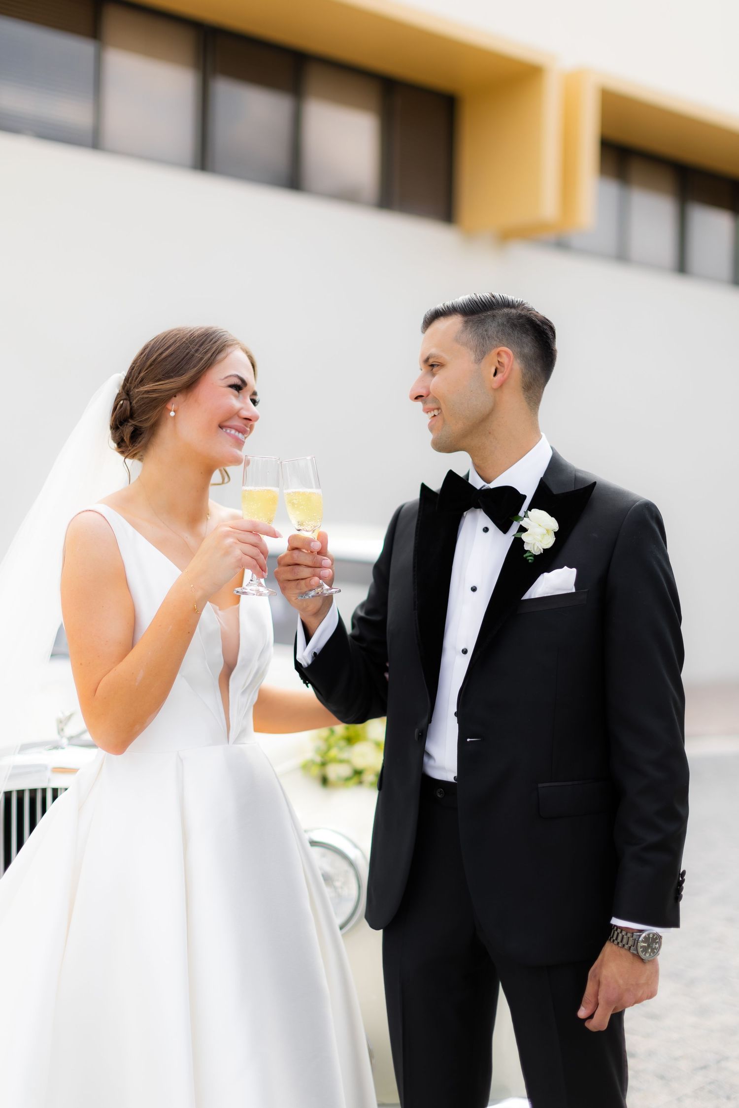 Couple in wedding attire sharing champagne outdoors.