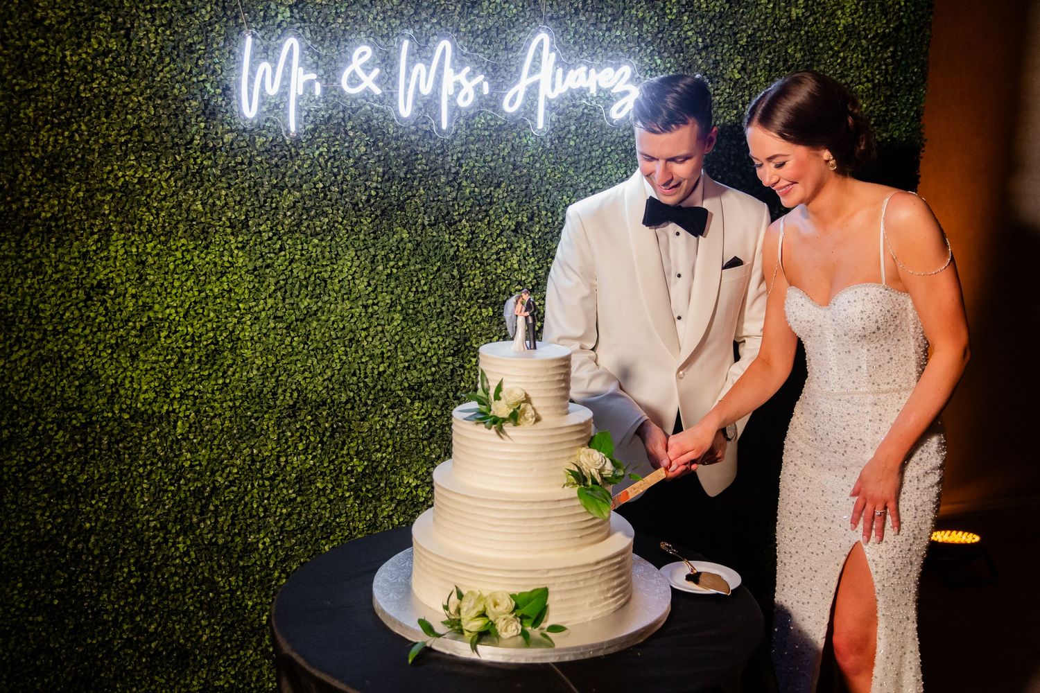 Couple cutting their wedding cake together under illuminated name sign.