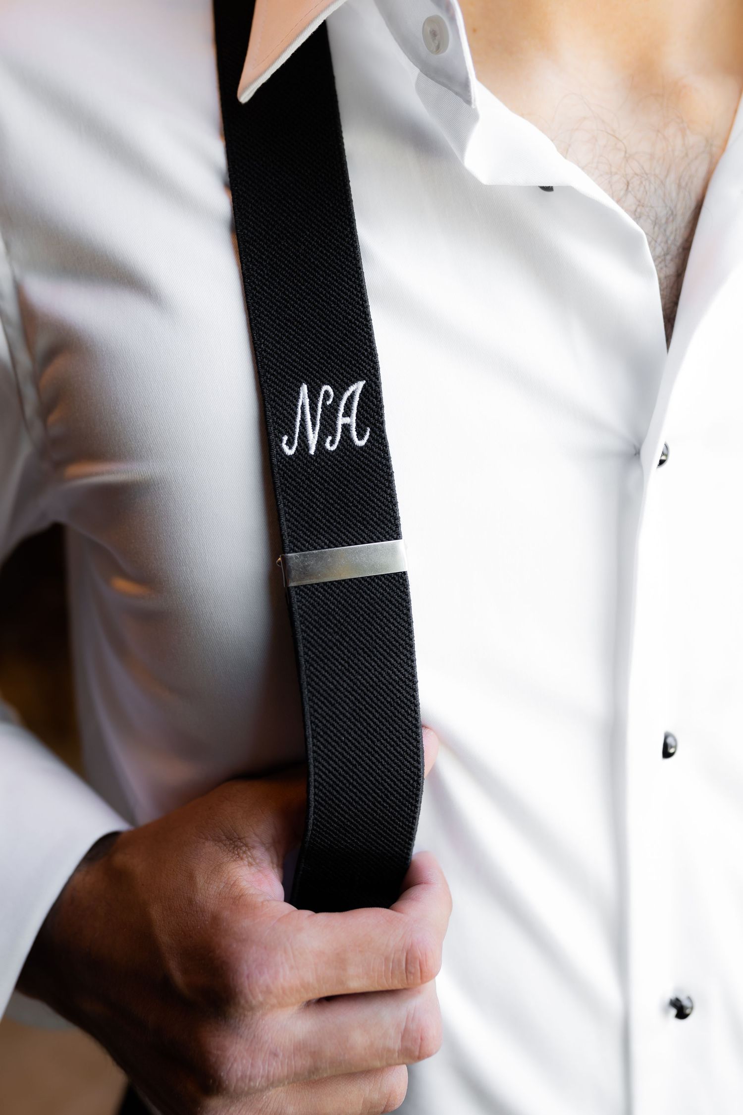 Close-up of monogrammed black suspenders against white shirt.