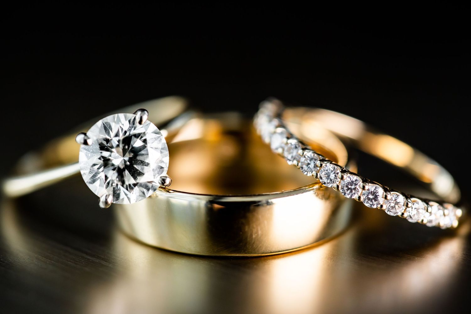 Closeup detail shots of sparkling diamond engagement rings and wedding bands on dark background.