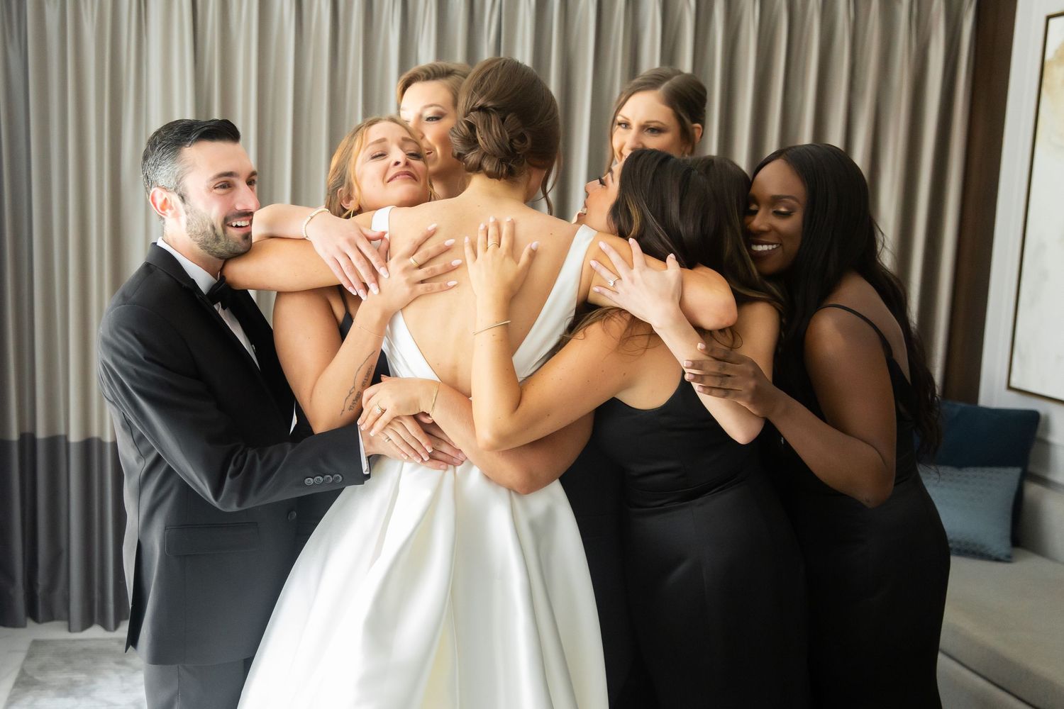 A wedding party wearing black and white outfits shares heartfelt reactions together.