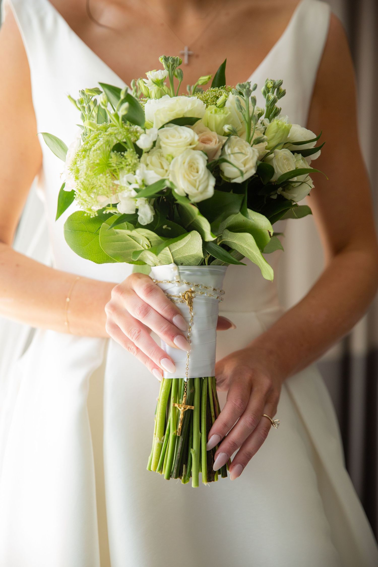 White and green wedding bouquet held against an elegant white dress.