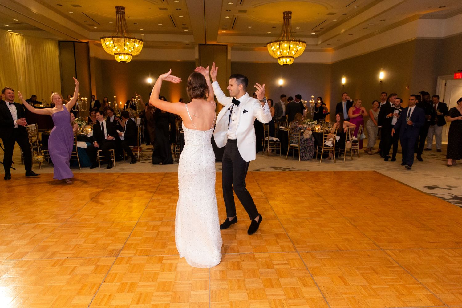Energetic dance party in an elegant ballroom with ornate chandeliers and hardwood floors.