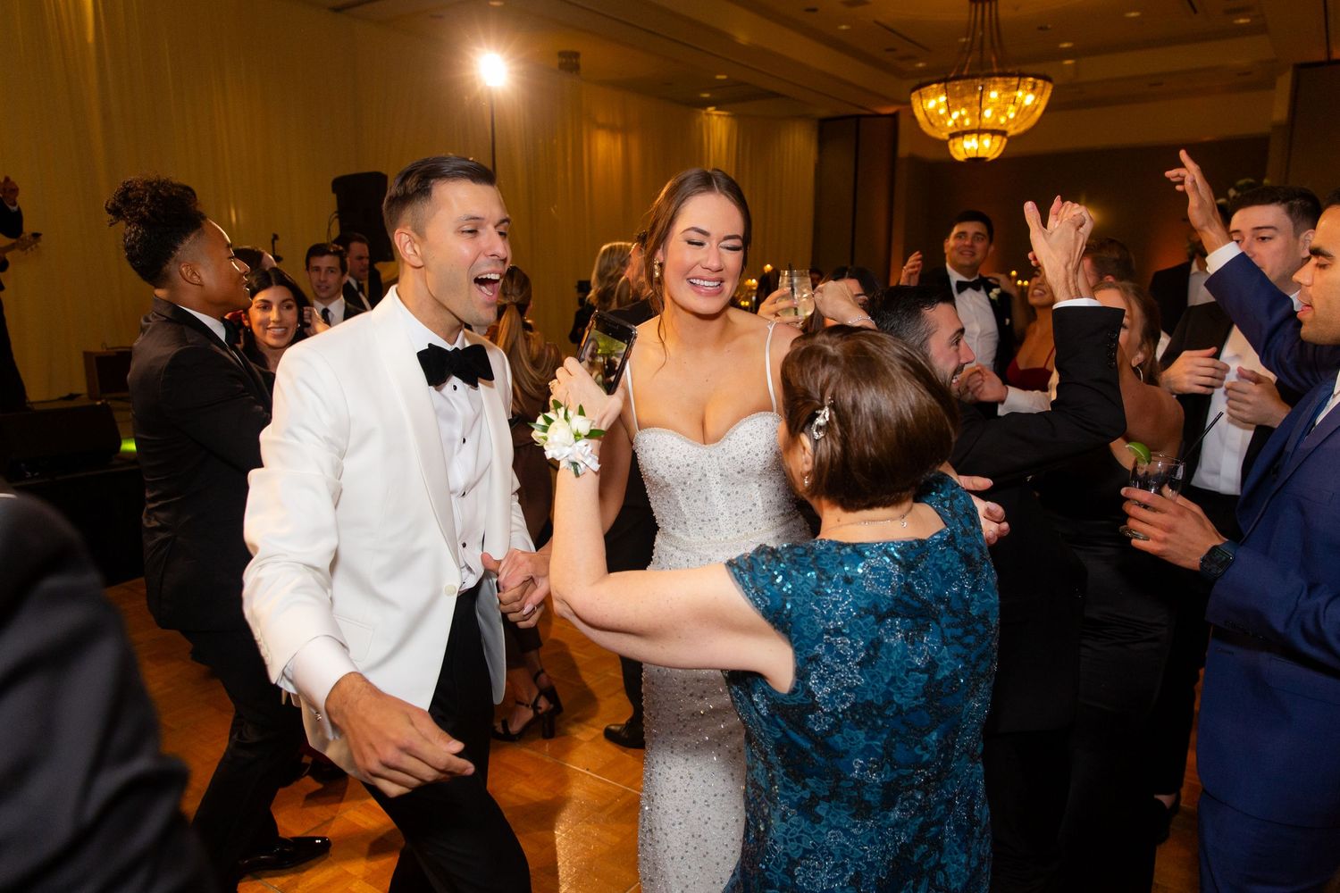 Lively wedding reception with guests dancing and socializing under golden chandeliers.