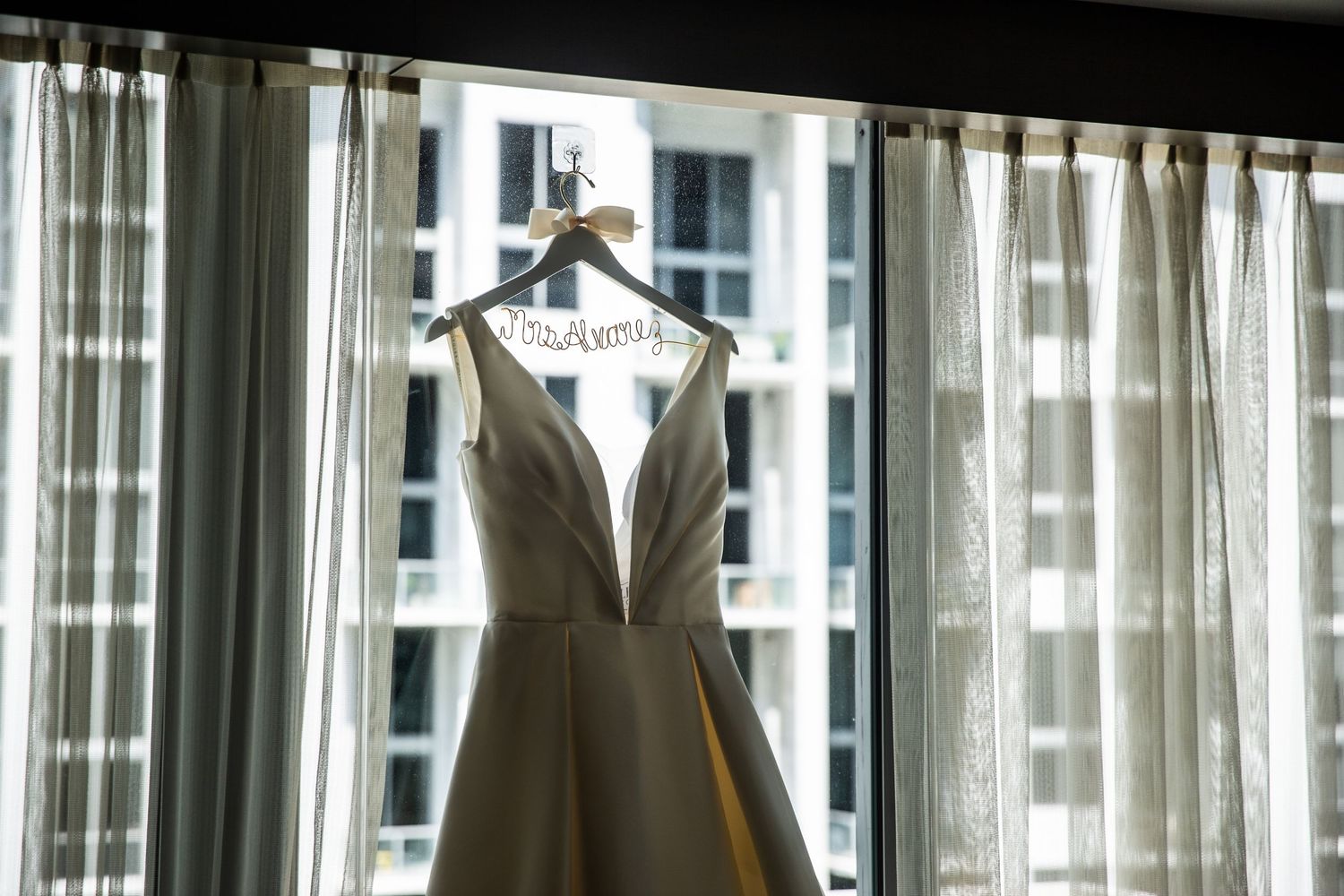 Wide panoramic view of hotel room windows with sheer curtains and city buildings in background.