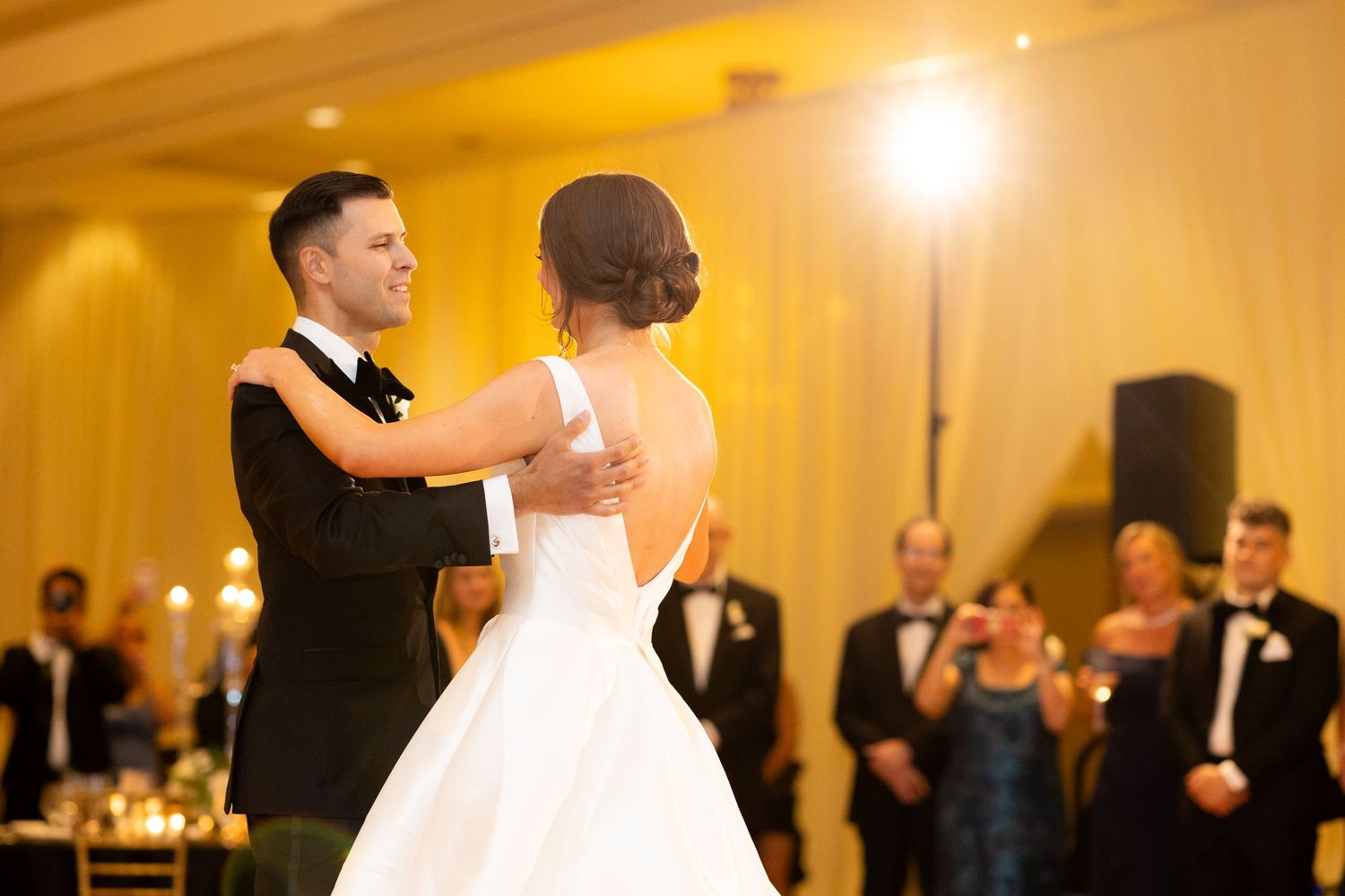 A couple dances together during their wedding reception with guests watching in the background.