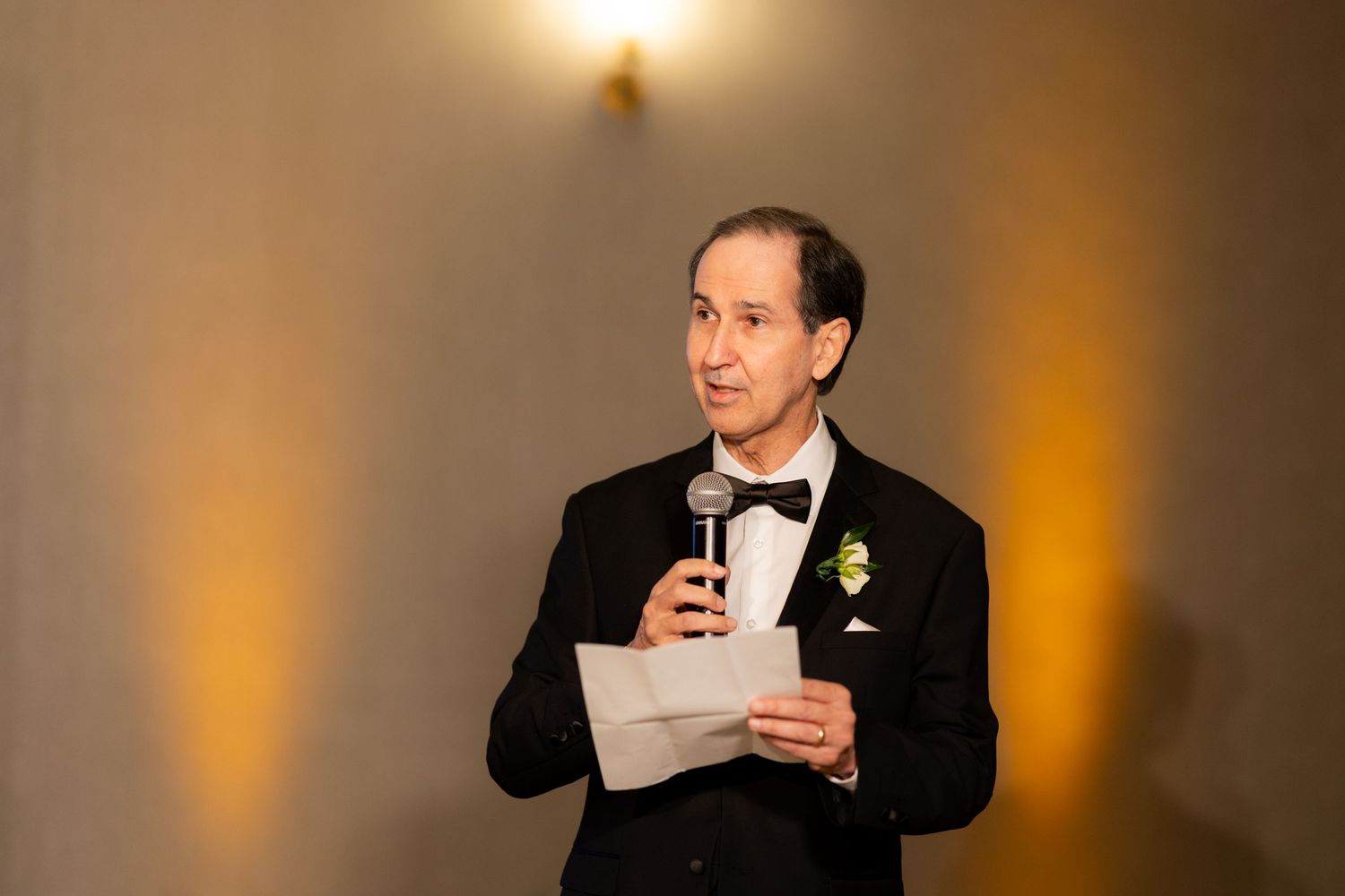 Wedding speeches being given at an elegant indoor reception with moody amber lighting.