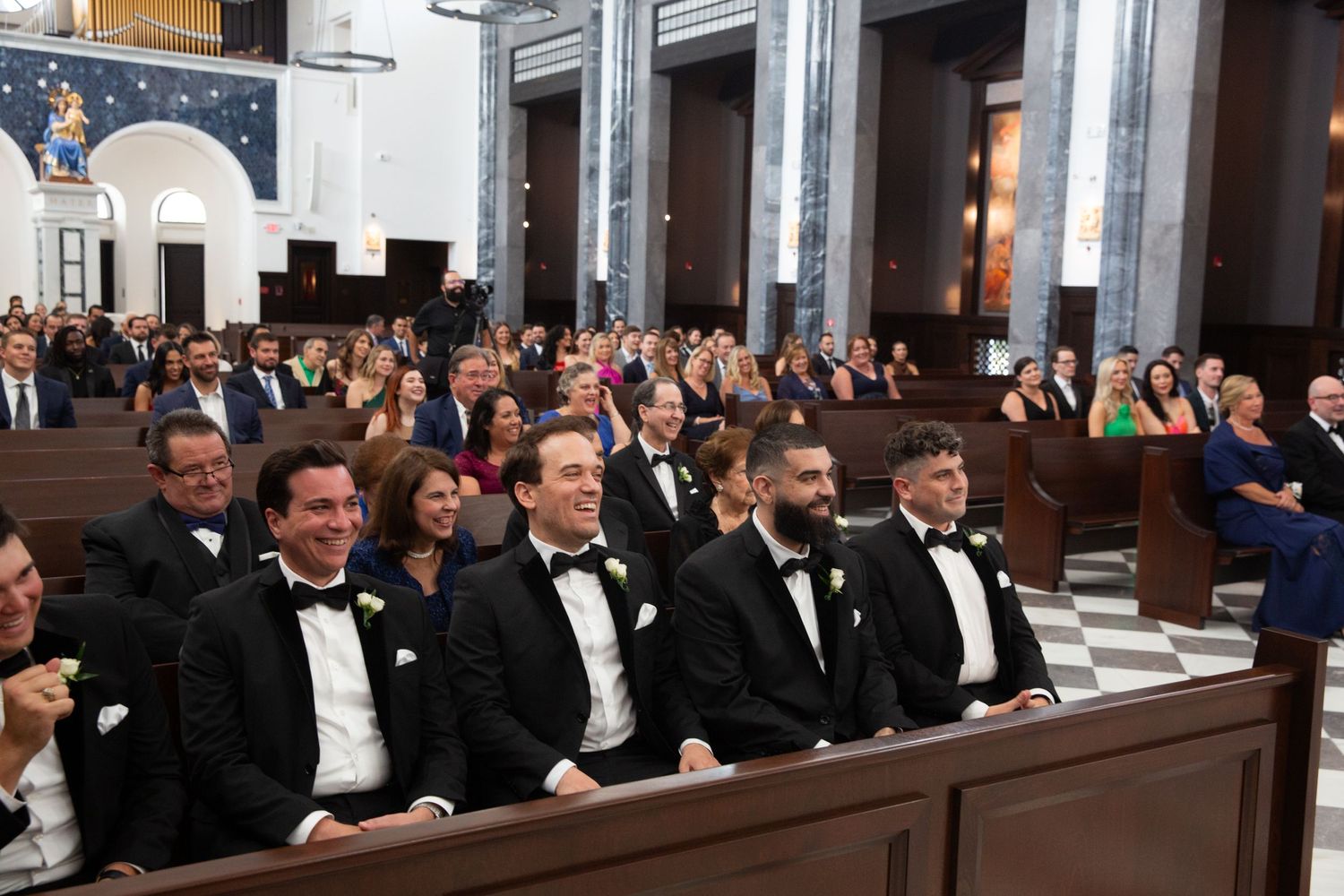Wedding guests fill church pews during traditional Catholic ceremony in elegant cathedral setting.