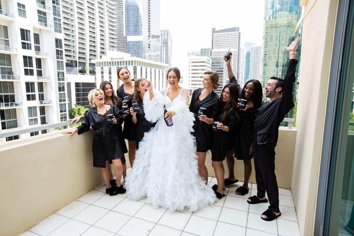 Wedding party celebrates on a rooftop terrace with city skyline view in background.