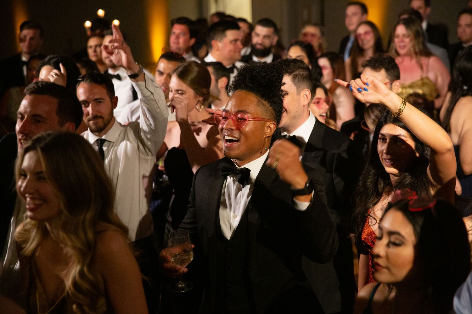 Crowd of formally dressed guests dancing and celebrating at wedding reception.