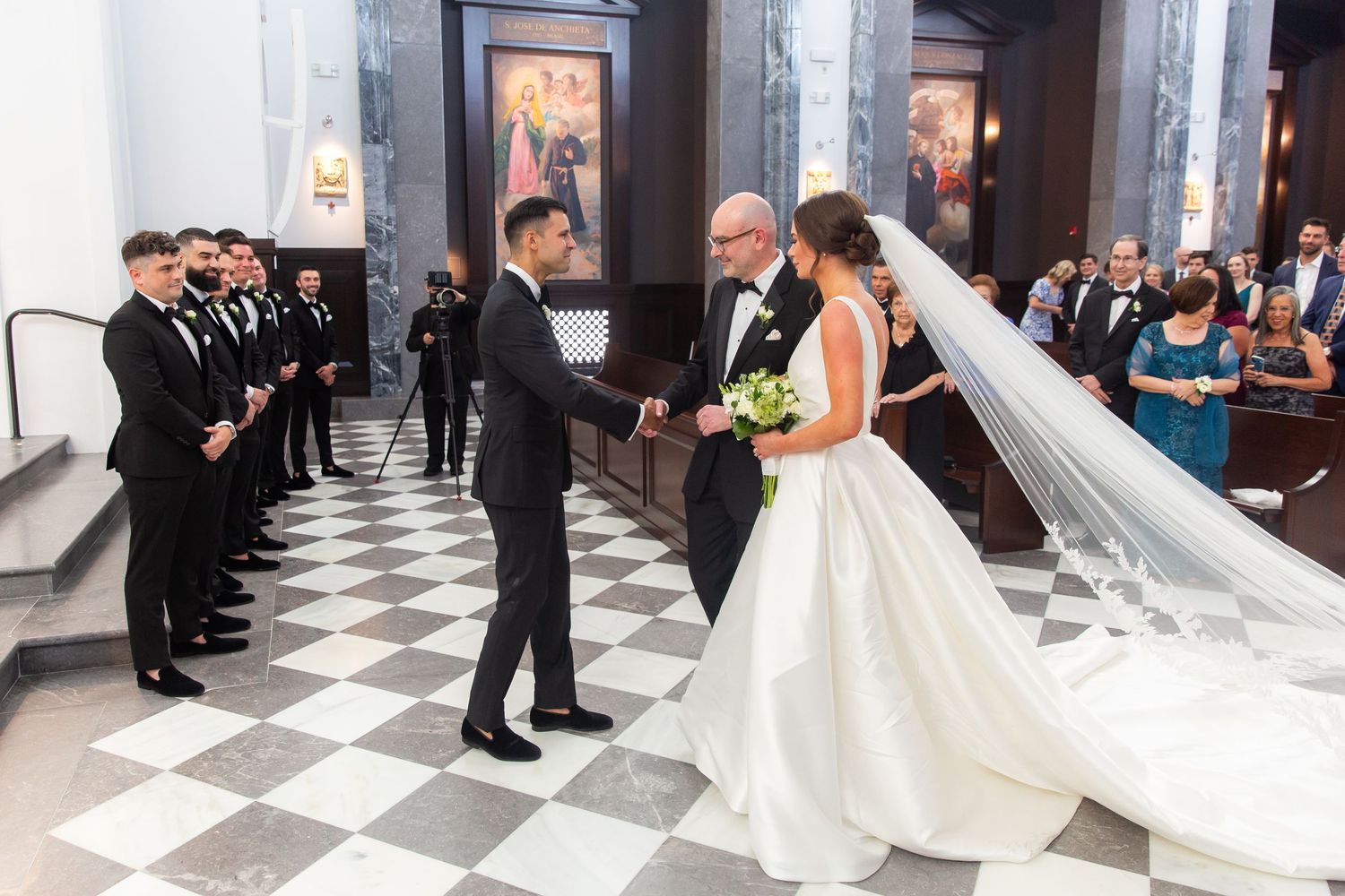 Wedding ceremony procession in elegant church with black and white checkered floor.