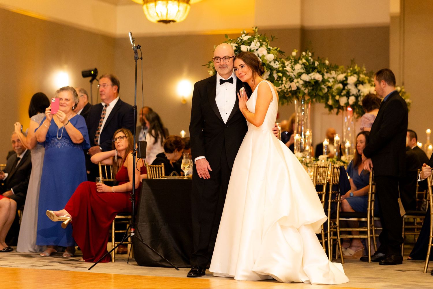 Wedding guests enjoying dances in an upscale ballroom with golden lighting.