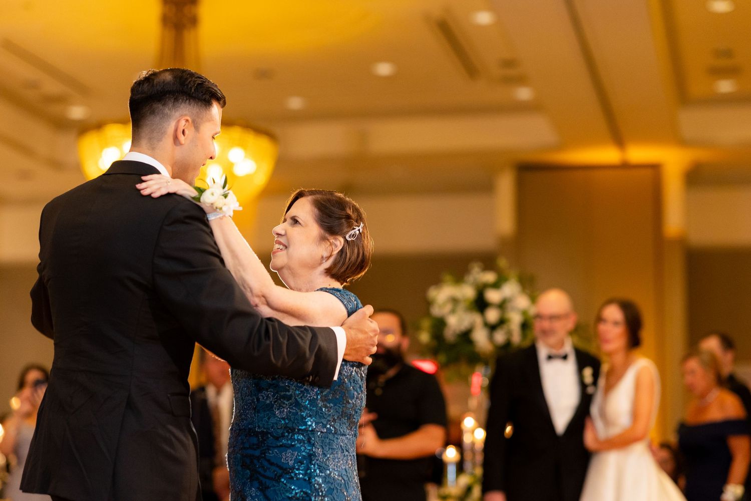 Formal dance floor scene at wedding reception with guests in black tie attire.