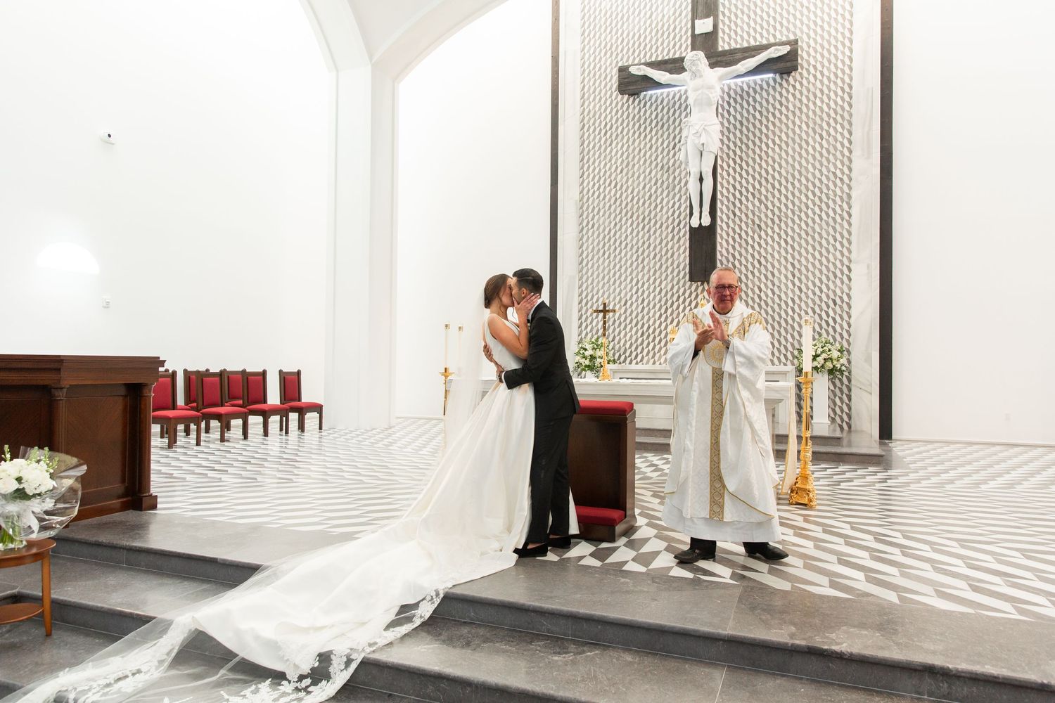 A wedding couple stands beneath a large wall crucifix during their church ceremony.