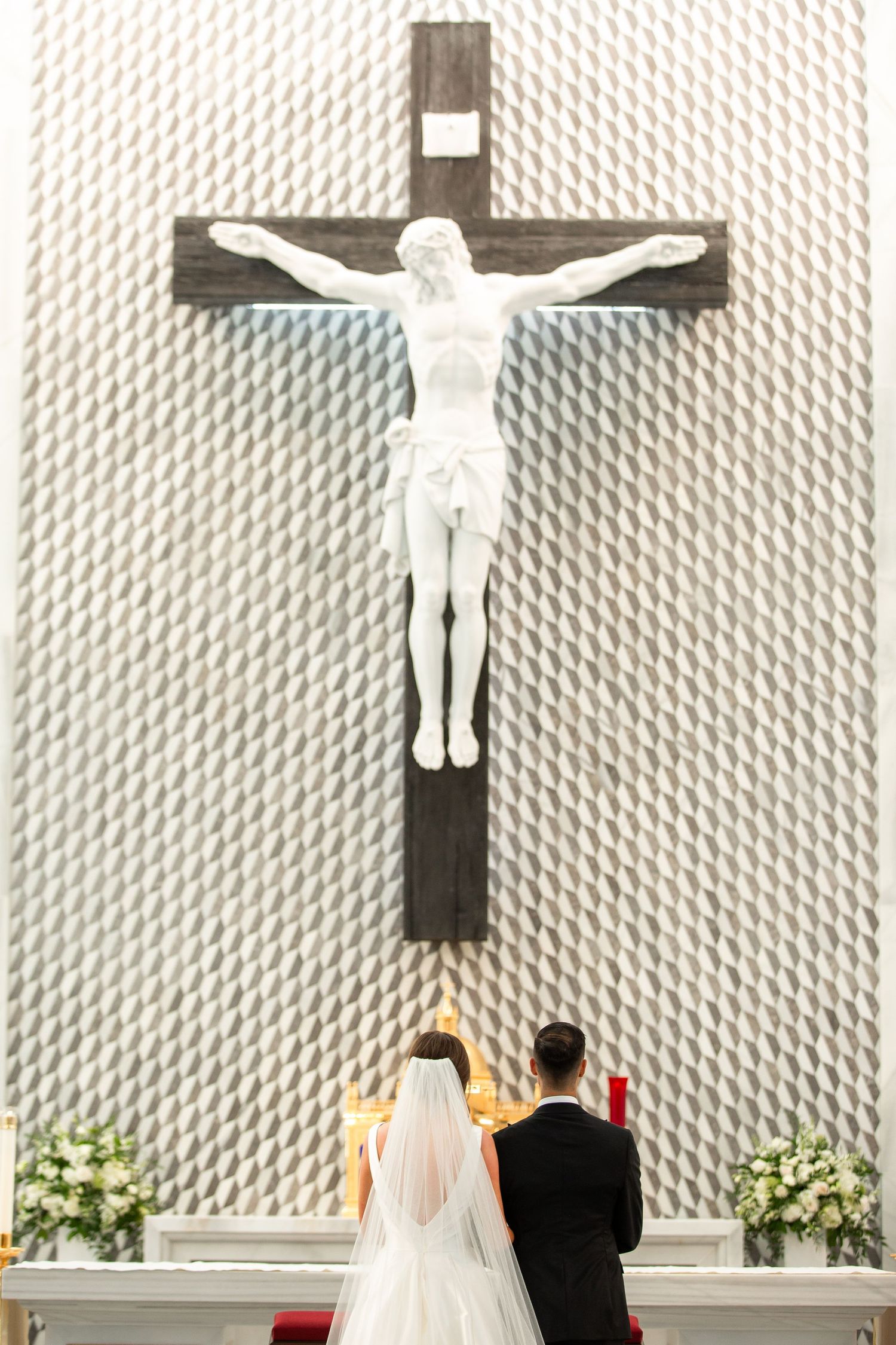 Modern church interior with white textured walls and large crucifix during wedding ceremony.