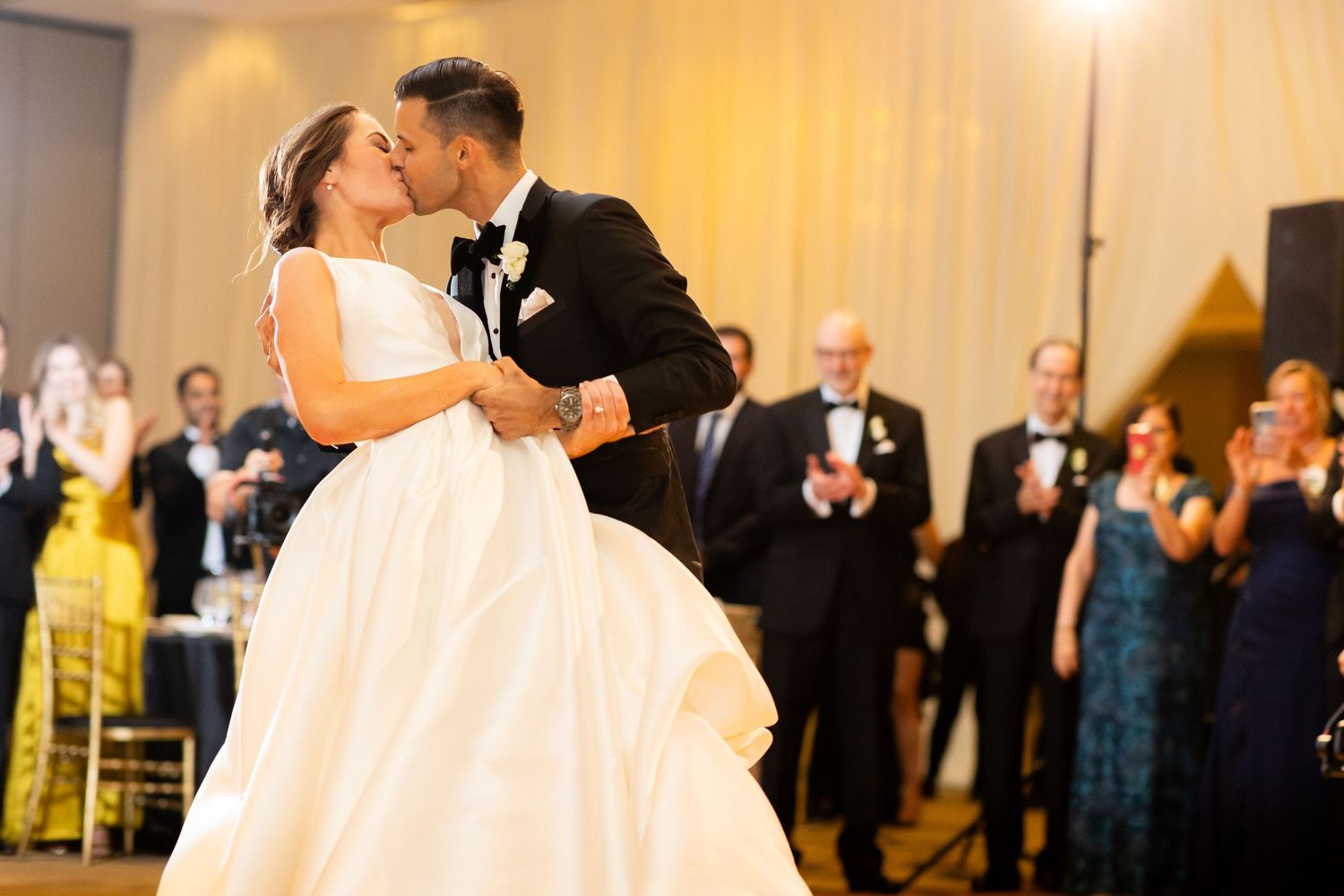 A romantic dip during a wedding first dance with guests watching in the background.