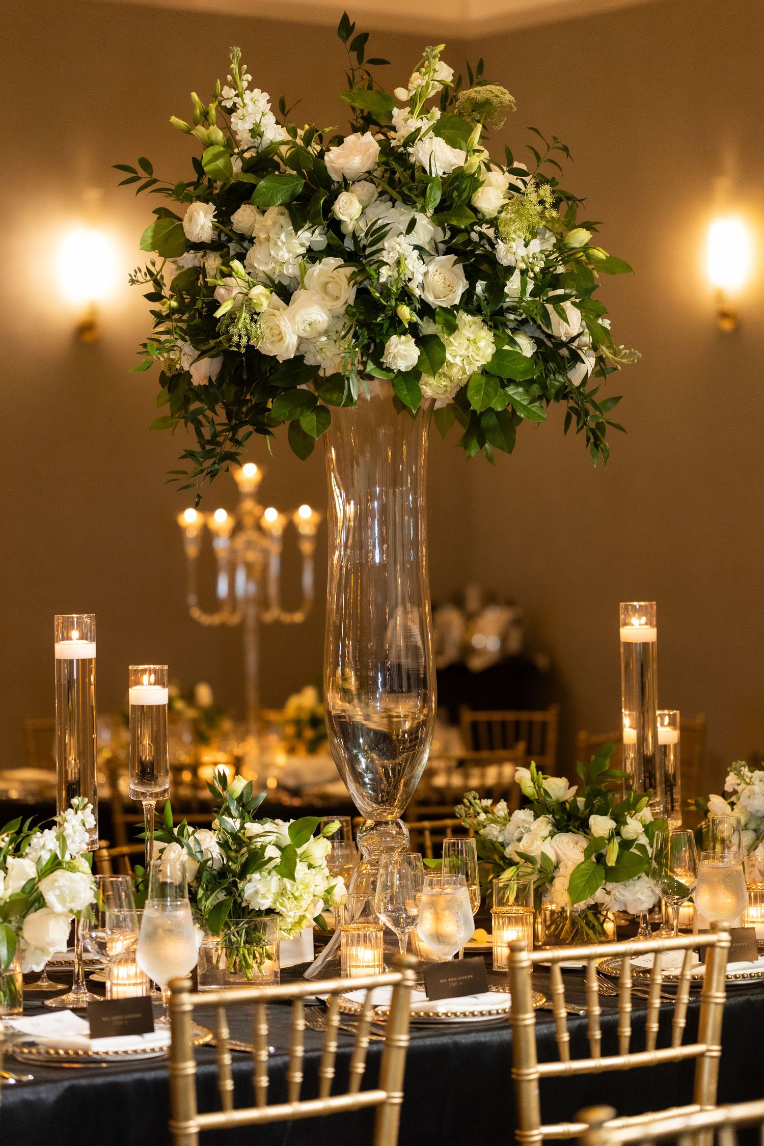 Luxurious wedding table settings with tall white floral arrangements and gold-rimmed charger plates.