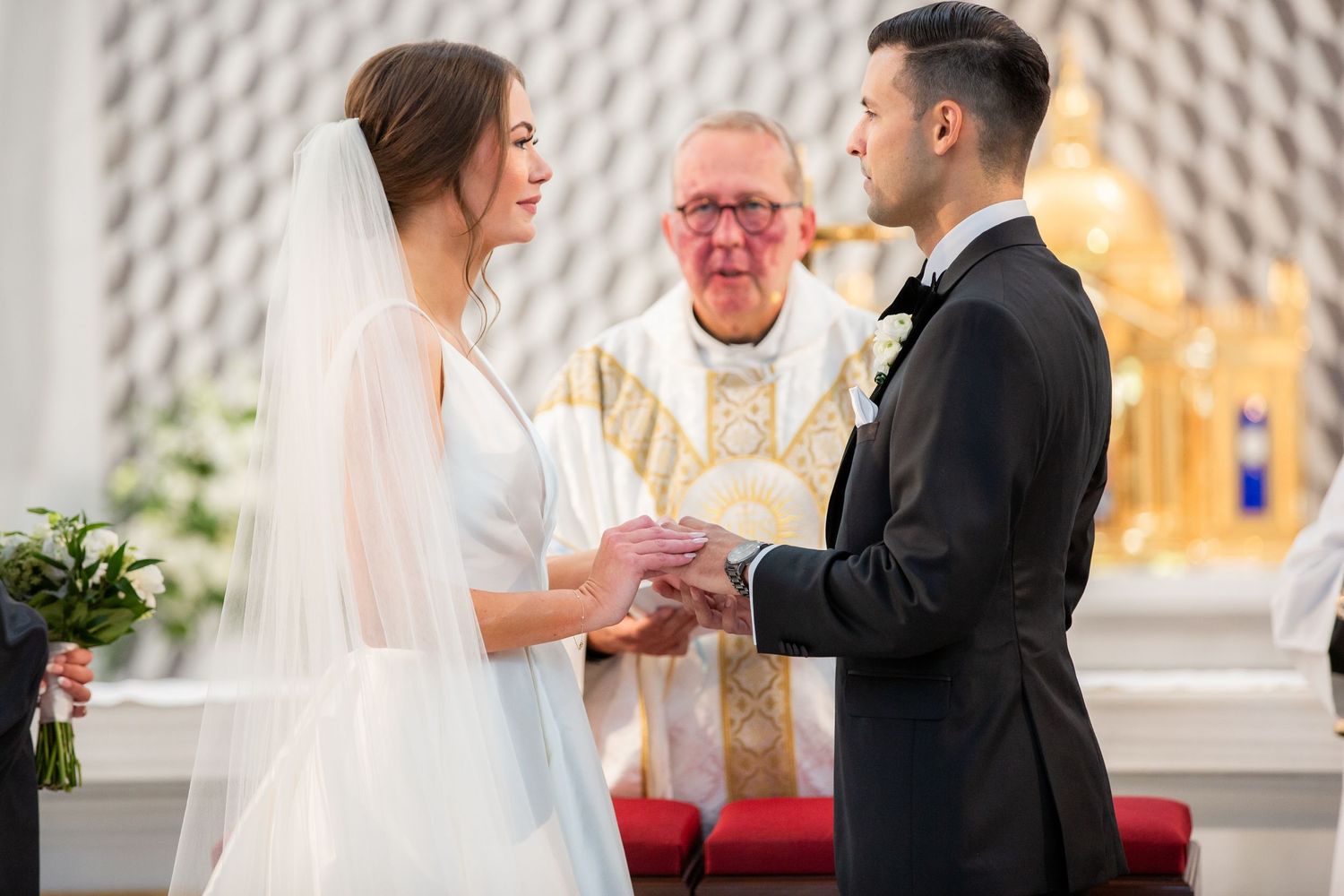 Wedding ceremony taking place at modern church altar with textured white wall backdrop.