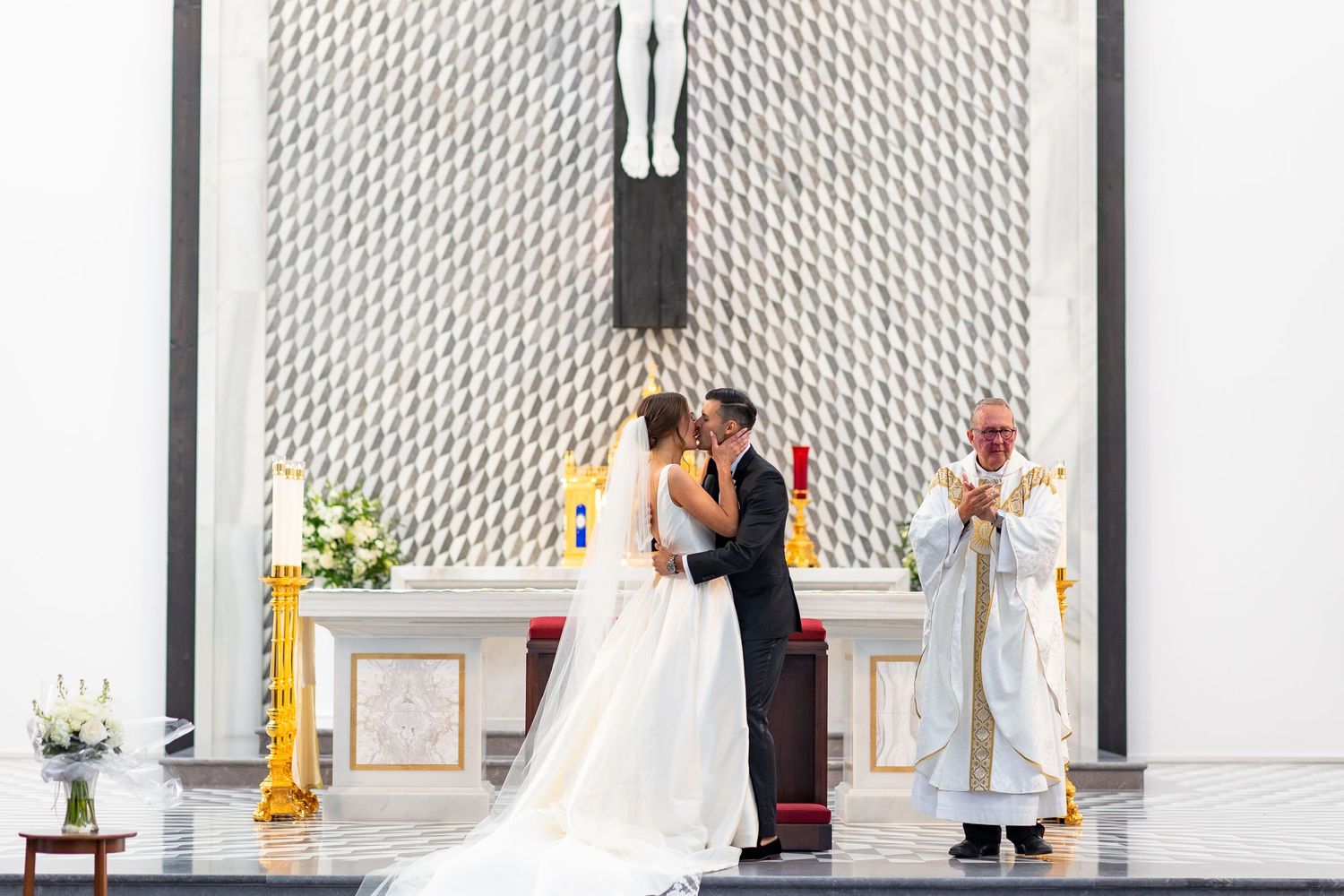 A wedding couple embraces during their ceremony in front of a geometric patterned wall.