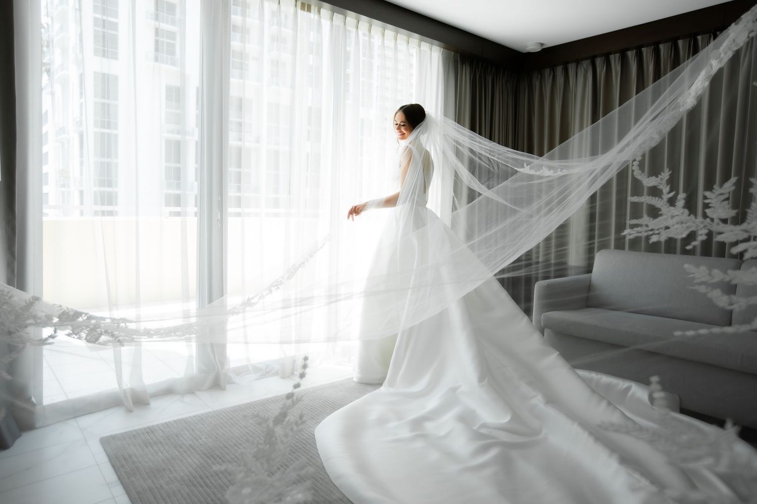 Bride's flowing veil creates dreamy silhouette against bright window light.