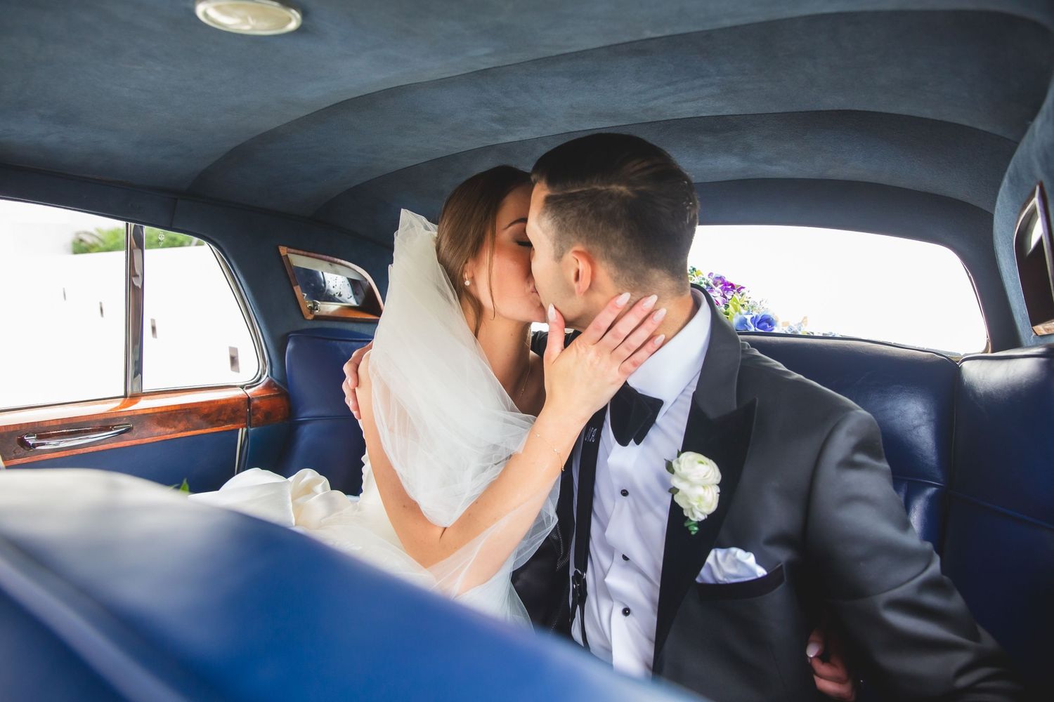 Wedding couple embracing in back seat of classic car with blue interior.