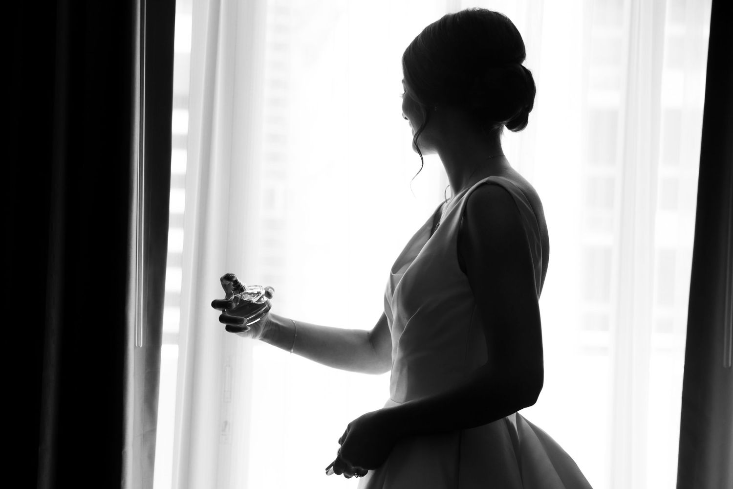 Silhouette of a bride getting ready by a bright window on her wedding day.