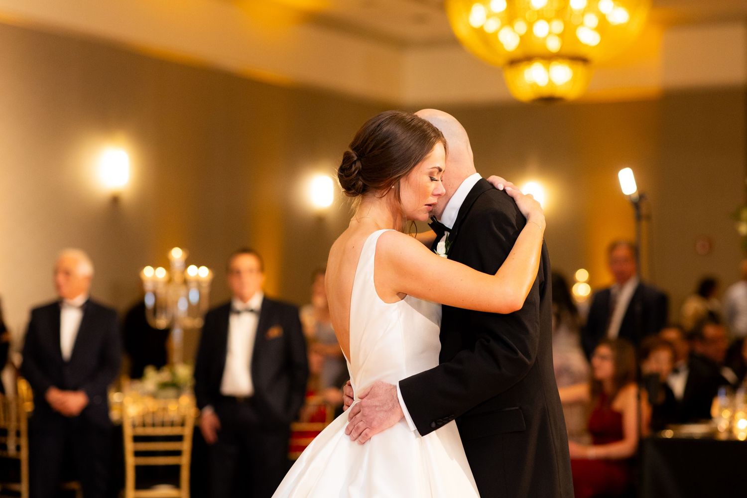 Guests dancing during an elegant wedding reception with chandeliers and warm ambient lighting.