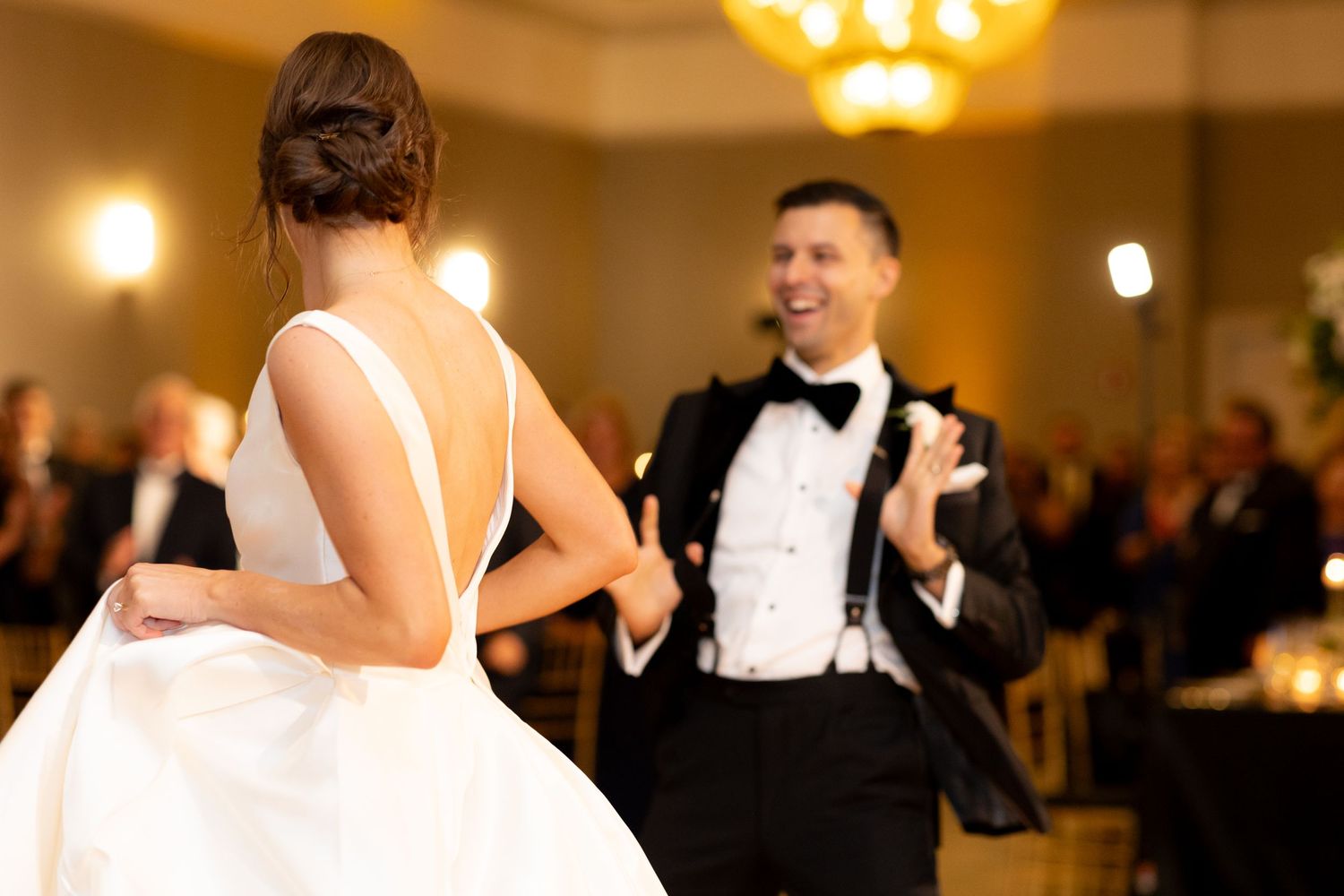Newlyweds dancing together at their reception with warm lighting and guests in the background.