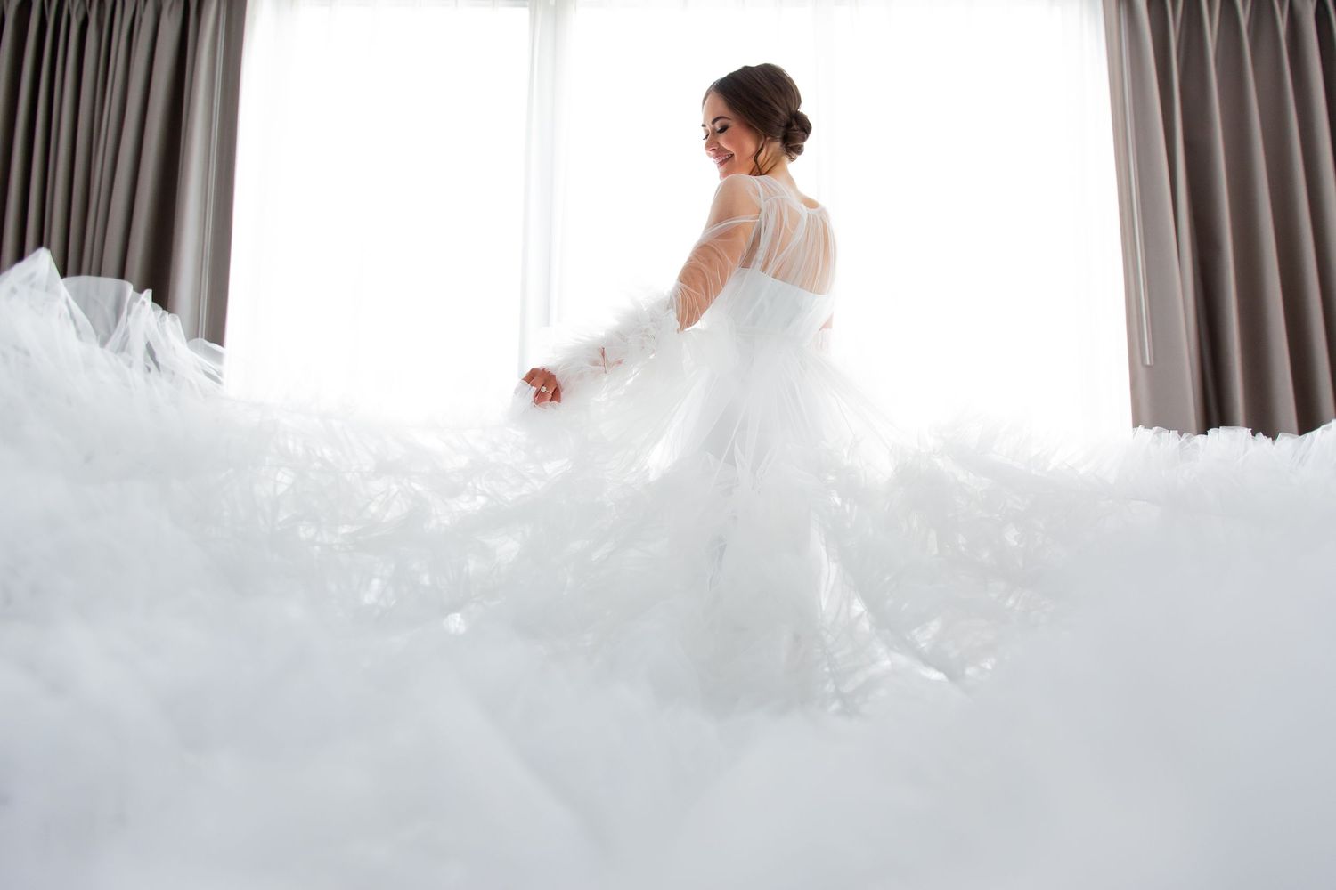 A stunning wedding dress with layers of tulle fabric flows elegantly across a bright indoor space.
