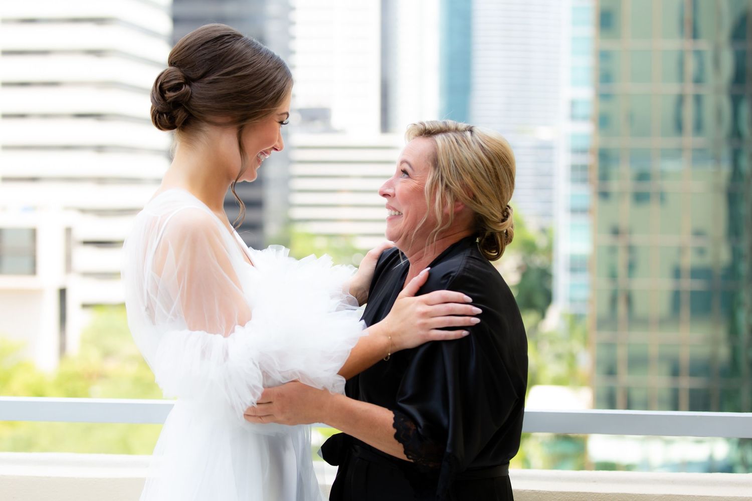 Joyful wedding day interactions captured on a modern high-rise balcony with cityscape backdrop.
