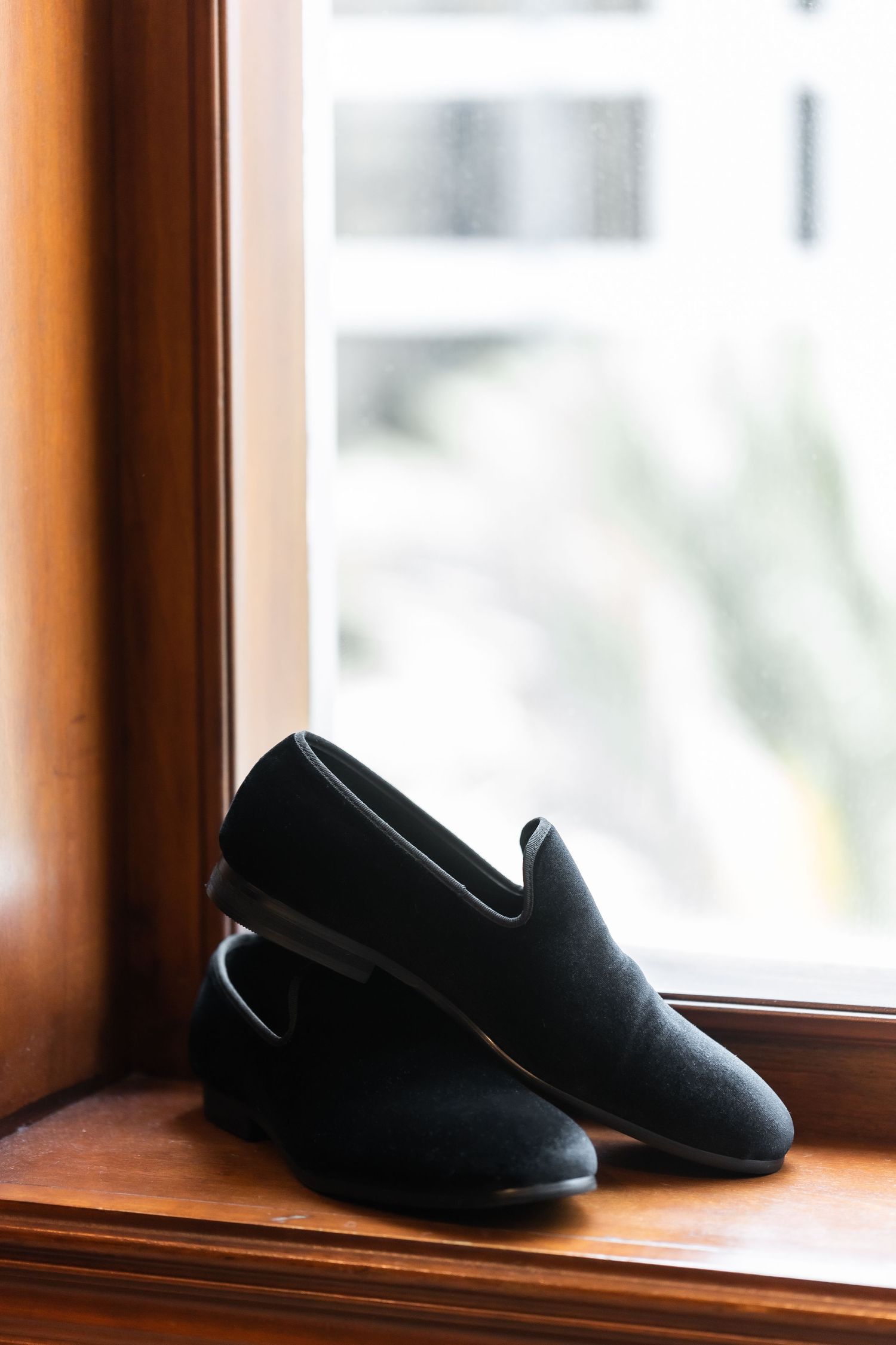 Black formal loafers sitting on wooden windowsill.