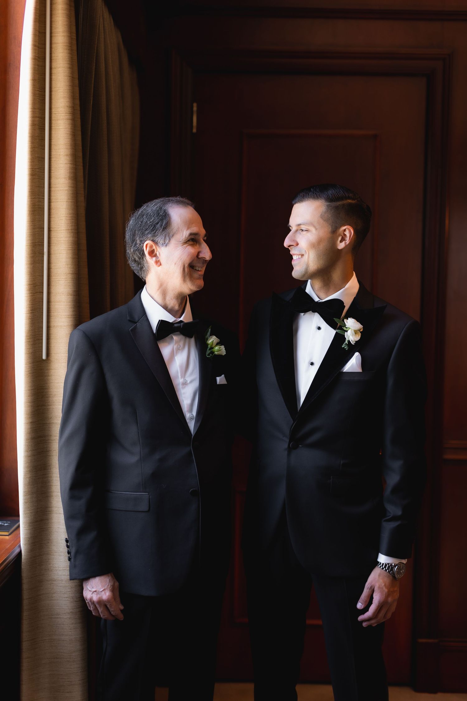 Wedding party members in formal attire interact in an elegant room with natural lighting.