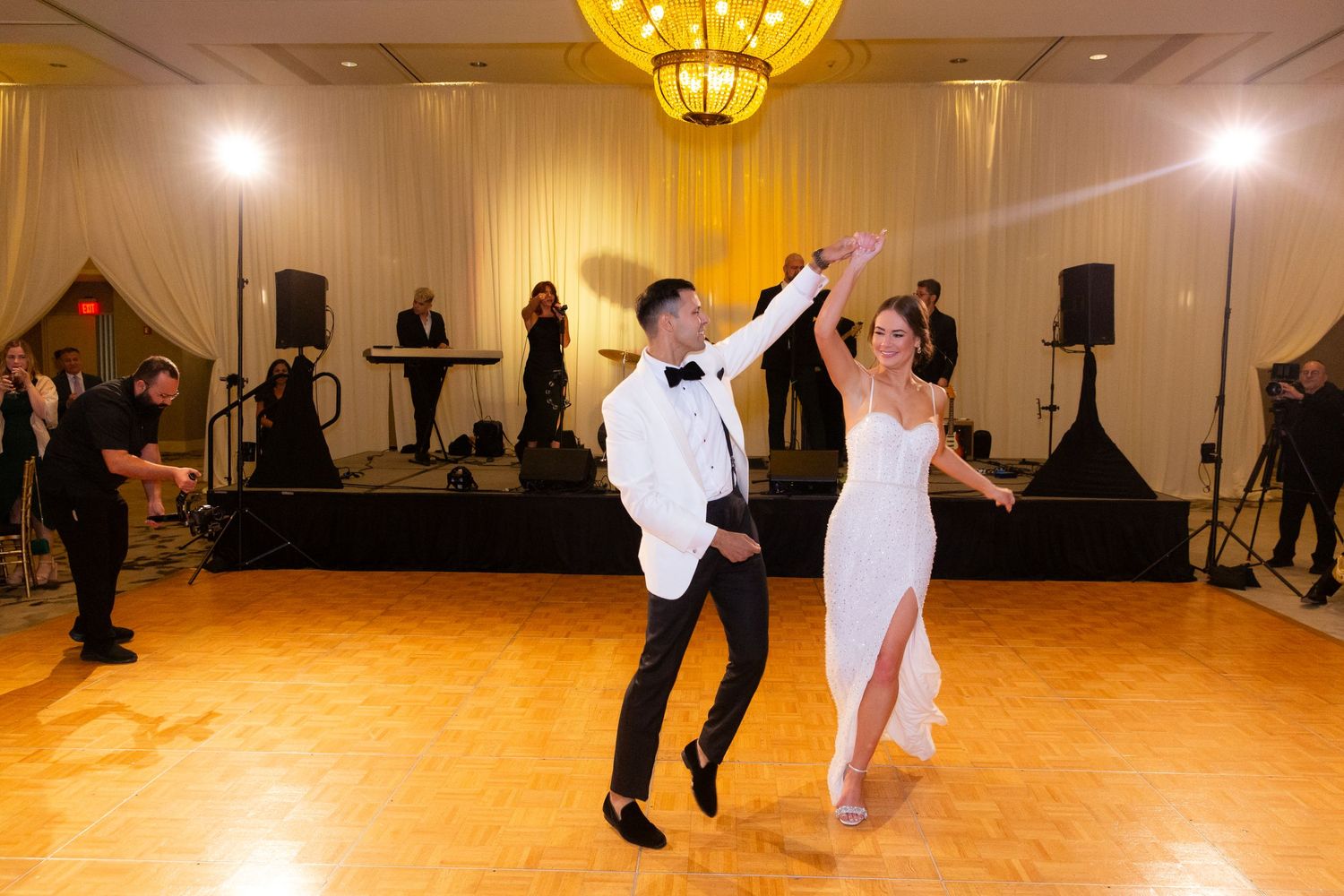 Couples dancing energetically at a wedding reception in a golden-lit ballroom.