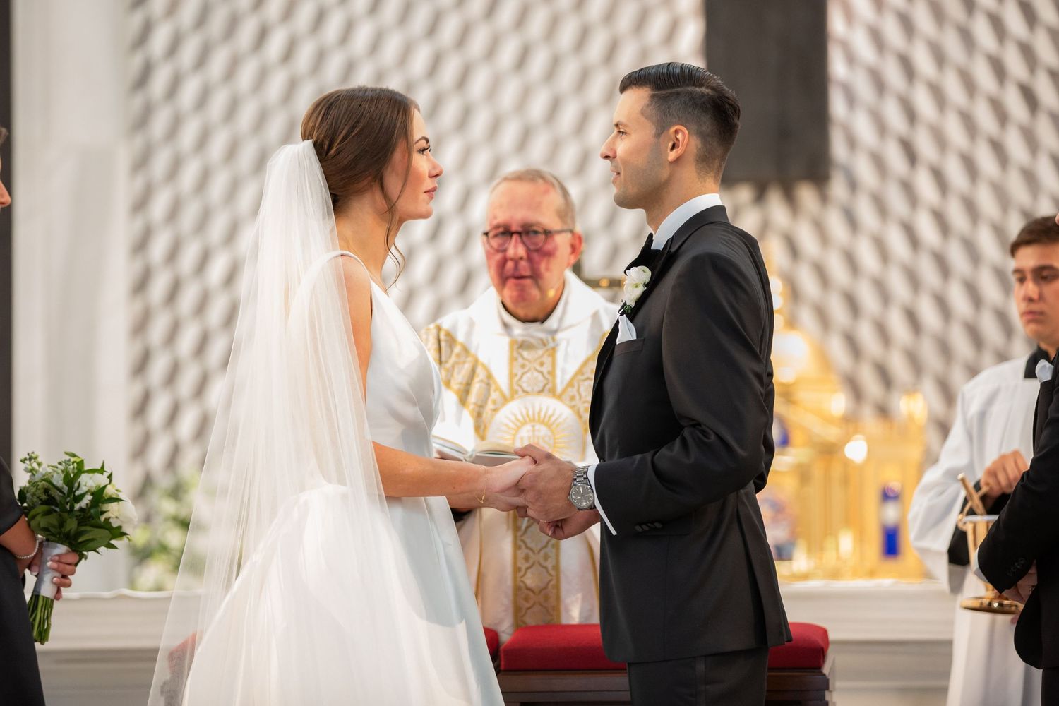 Traditional Catholic wedding ceremony with priest officiating in modern church interior.
