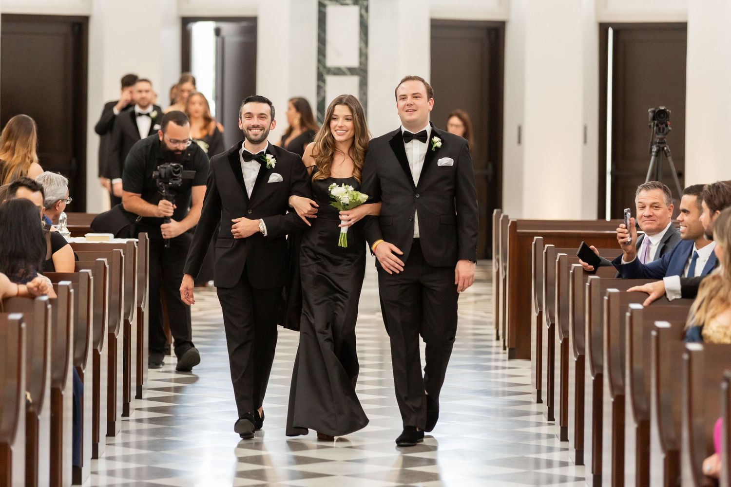 Wedding party members walking and laughing together down a formal church aisle.